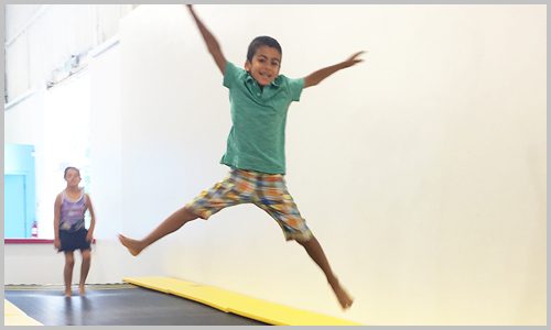 A smiling student jumps down the Tumble Track at AIM Gymnastics' Ajax location.